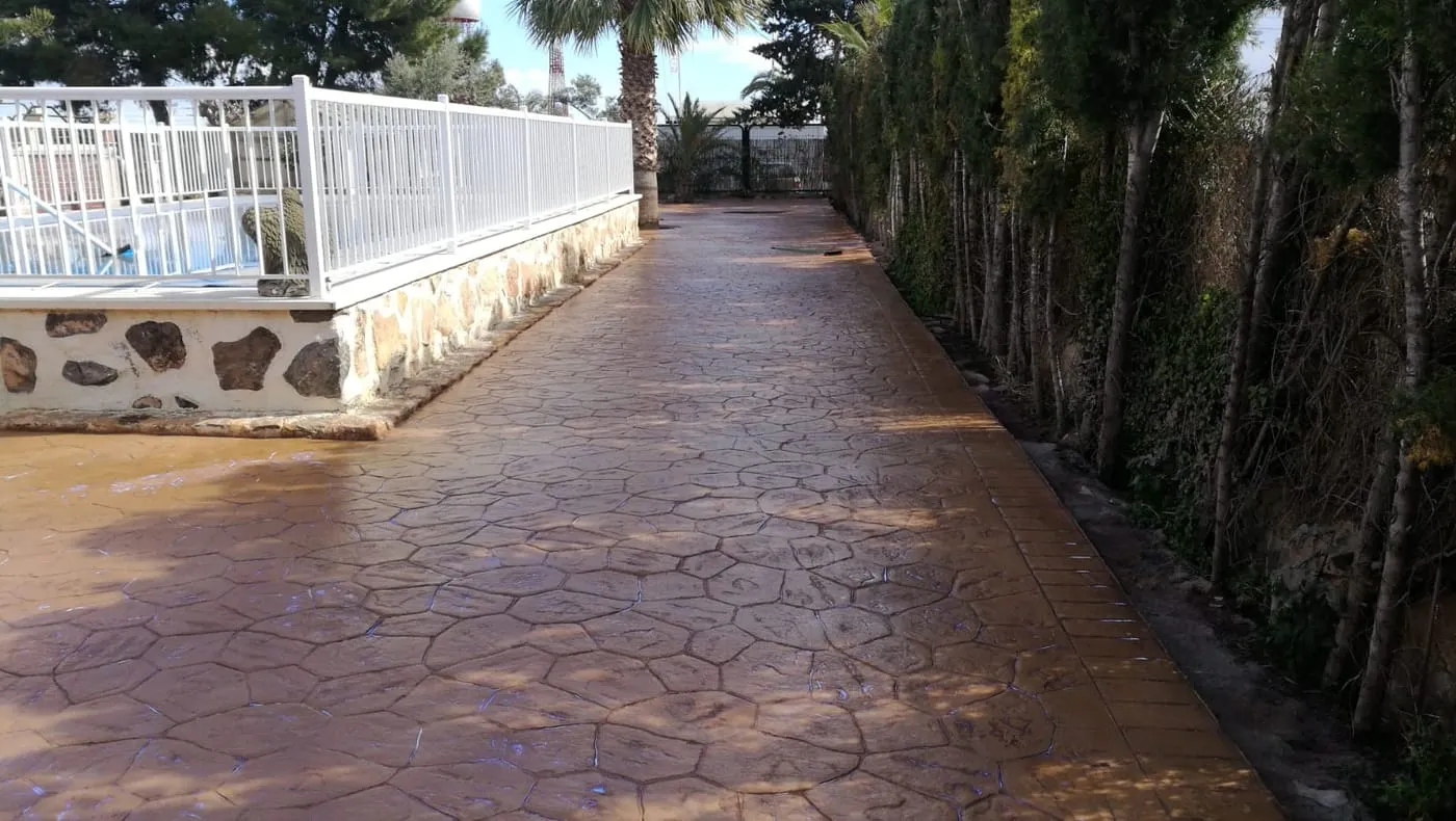Camino junto a la valla de una piscina en hormigón impreso con piedra irregular