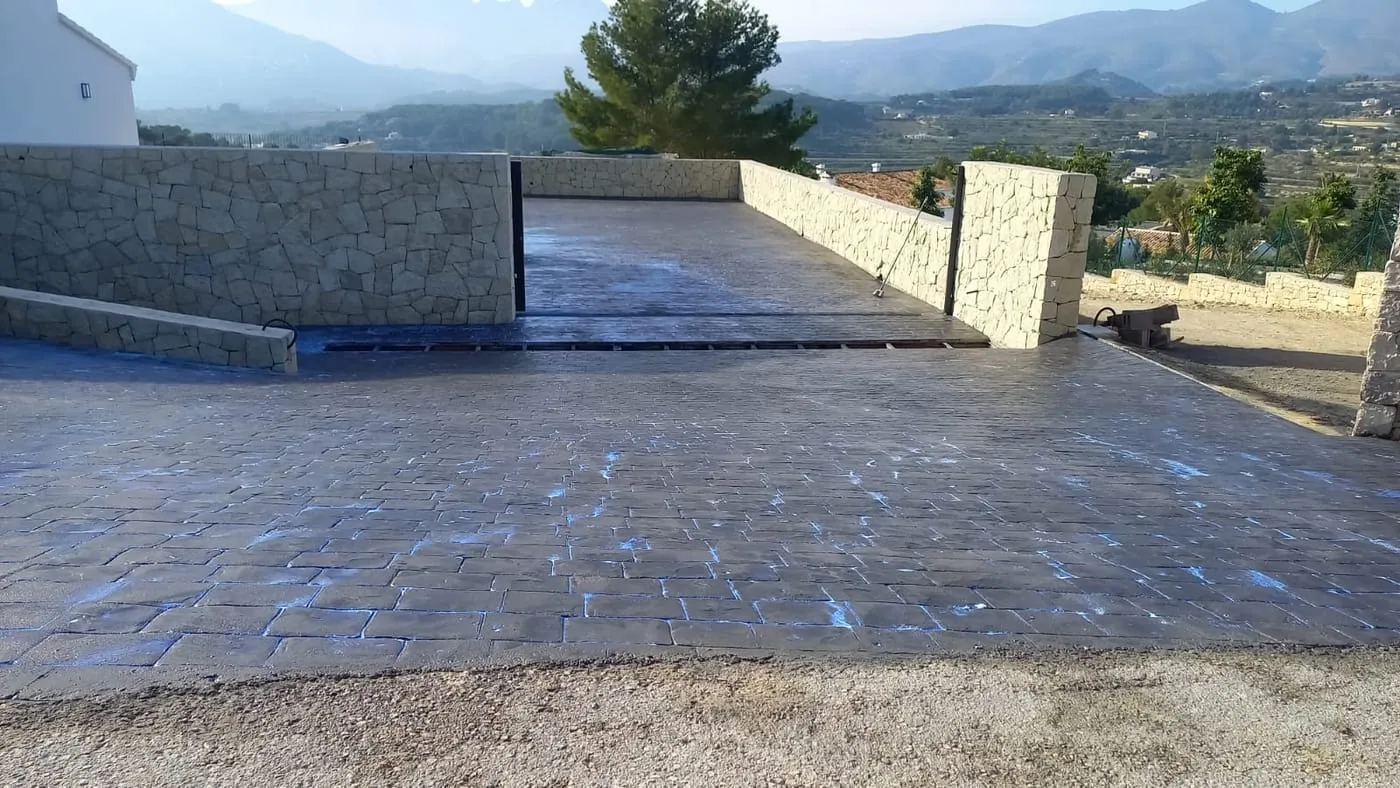 Entrada de parcela con muros de piedra y suelo de hormigón impreso