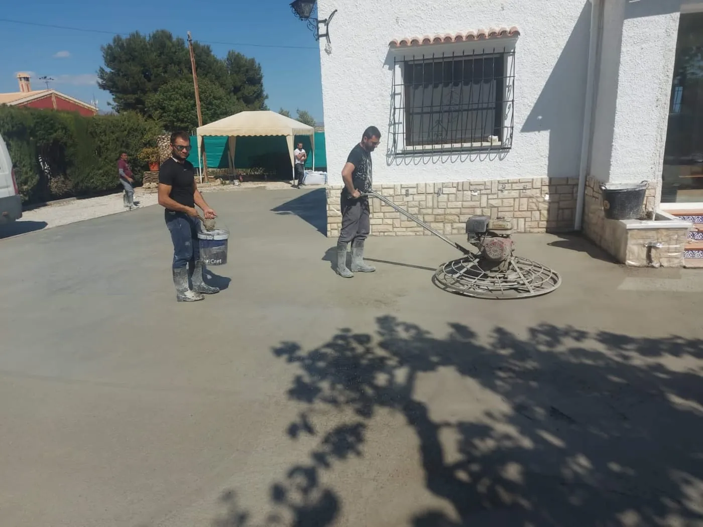 Dos operarios fratasando a máquina una solera de hormigón delante de una vivienda