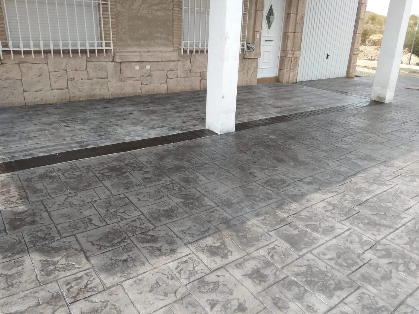 Porche de vivienda con hormigón impreso gris y molde de piedra