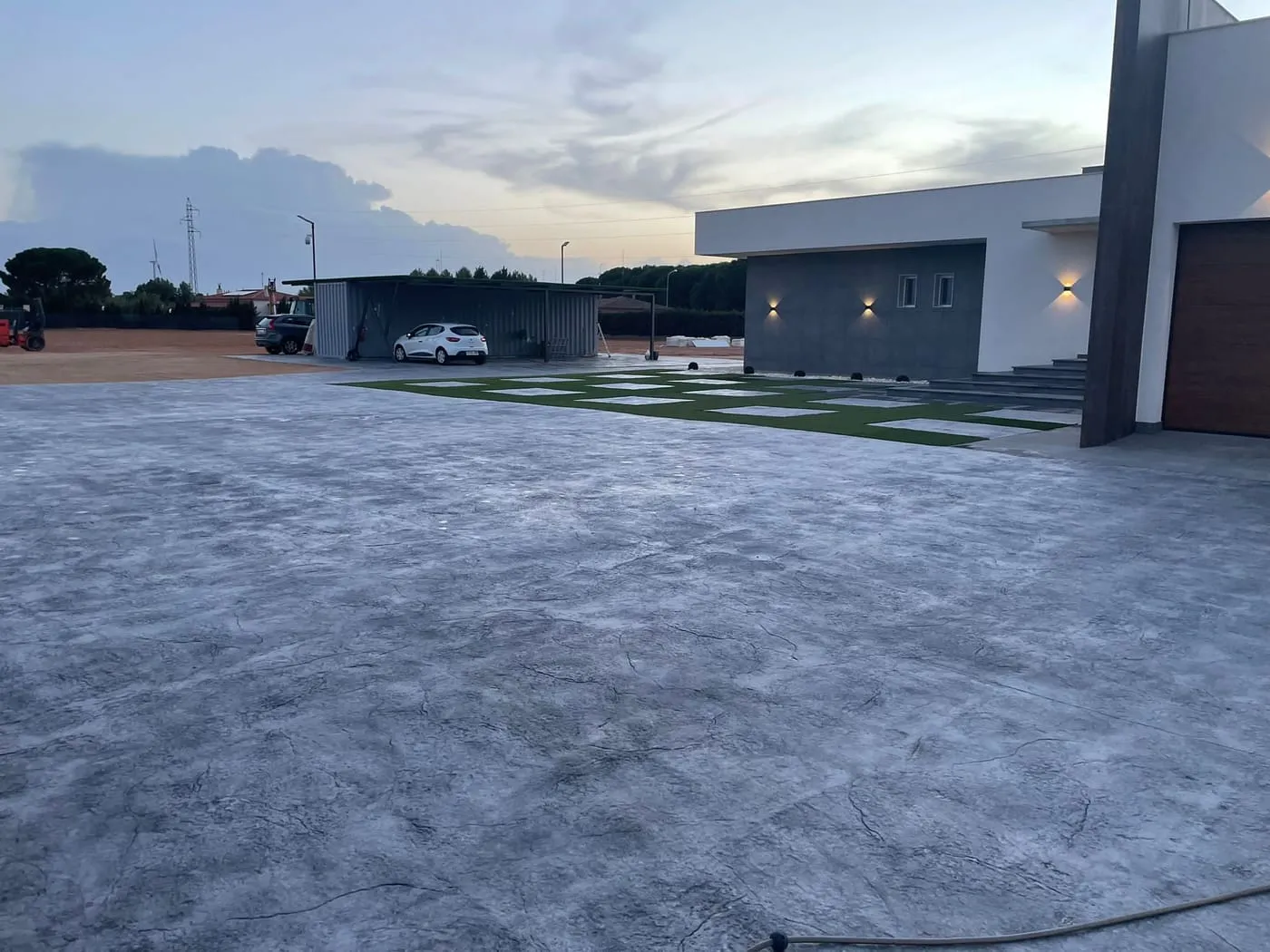 Explanada de hormigón impreso gris con franjas de césped delante de un chalet moderno